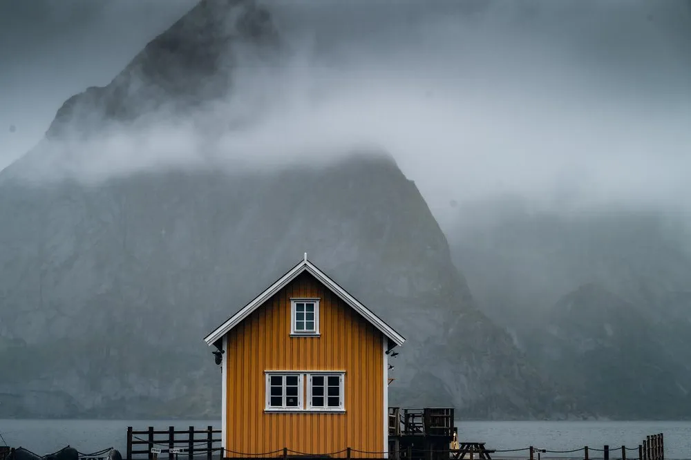 Close-up of the yellow fishing house in Sakrisøy in front of a fog-shrouded mountain