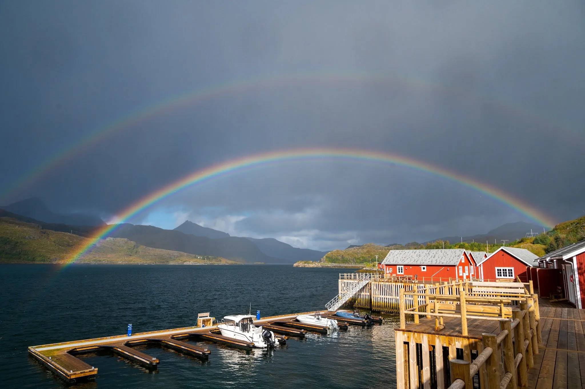 A double rainbow over a jetty and red fishing huts on the fjord