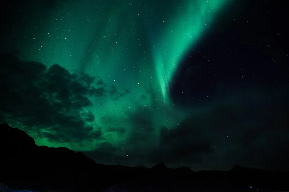 Nordlicht mit senkrechten Strahlen über dunklen Wolken und Bergkämmen