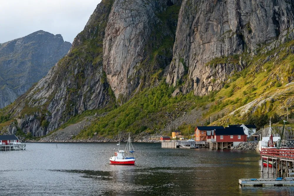 Ein rot-weisses Boot auf dem Wasser vor roten Fischerhütten und steilen Felswänden