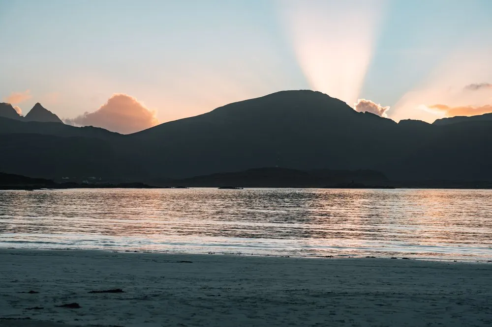 Sonnenstrahlen hinter einem dunklen Berg über dem Meer am Rambergstranda