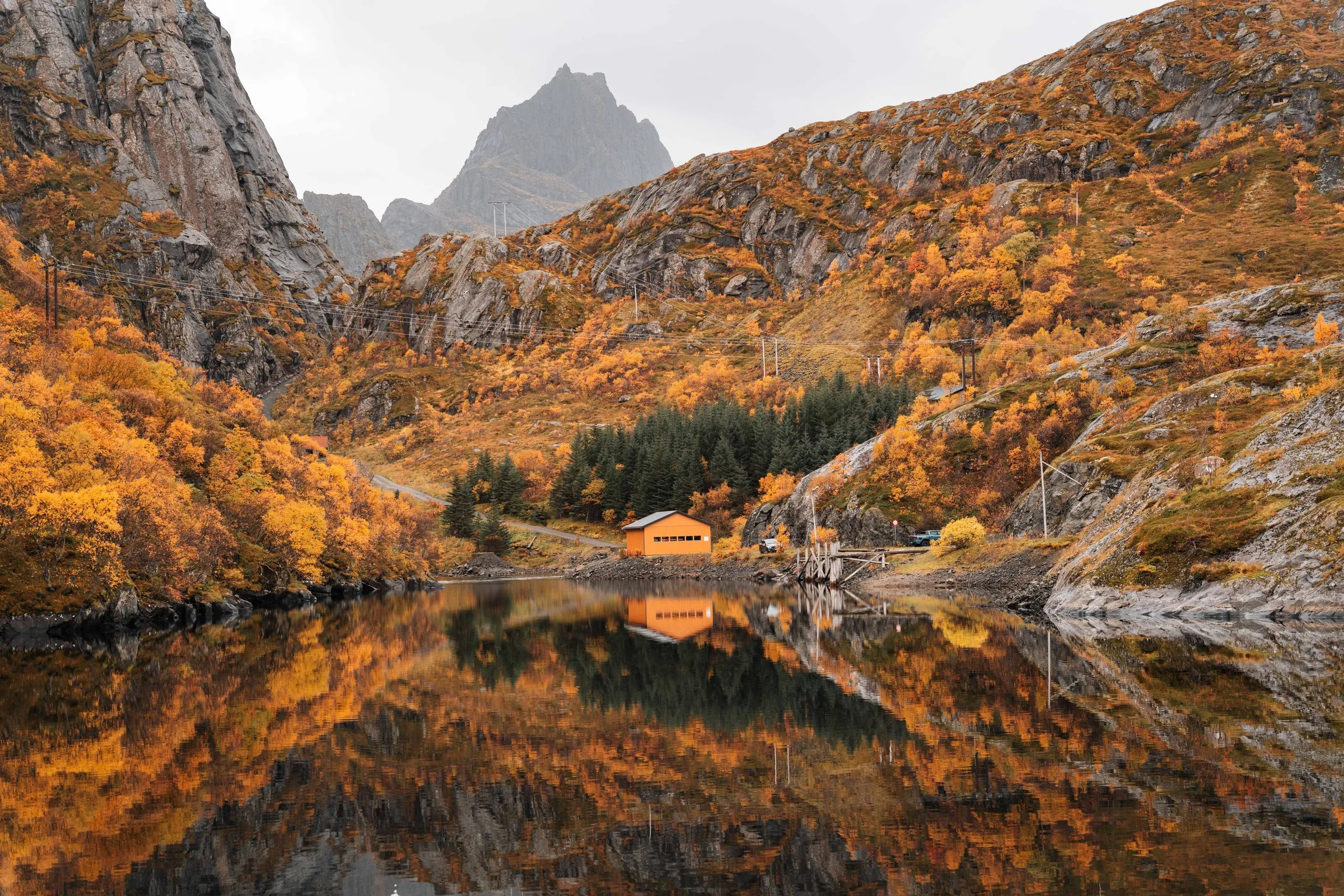 Ein oranges Haus am Ufer auf dem Weg zum Reinebringen, im stillen Wasser spiegeln sich herbstlich orange Hänge und graue Gipfel