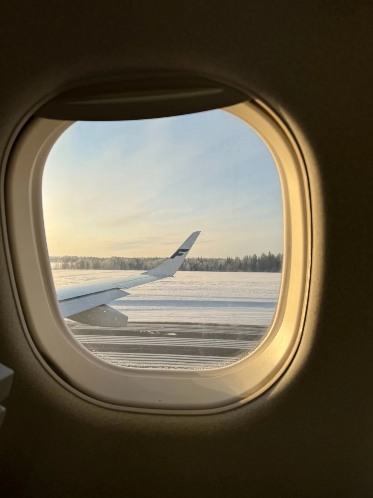 Blick durch das Kabinenfenster auf die Tragfläche über dem verschneiten Flugfeld in Kuusamo