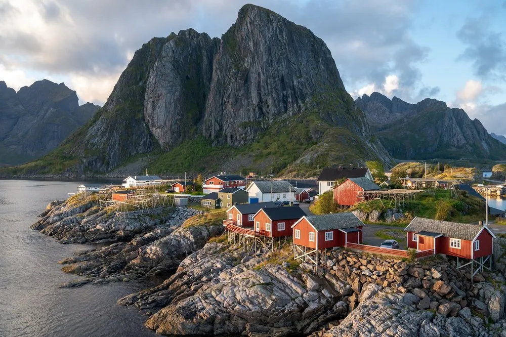 The fishing cabins of Hamnøy in warm light, the mountain massif behind them with clouds in the sky