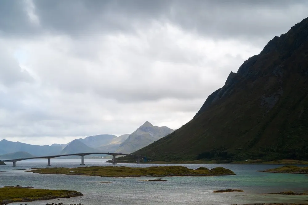 A long, gently curving bridge over an arm of the sea, a steeply sloping mountainside on the right, mountains in the haze on the left