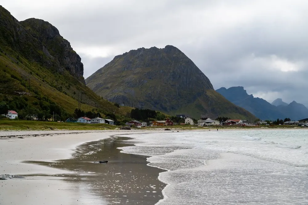 Wet sandy beach at Rambergstranda with waves running out, houses at the foot of a pointed mountain behind