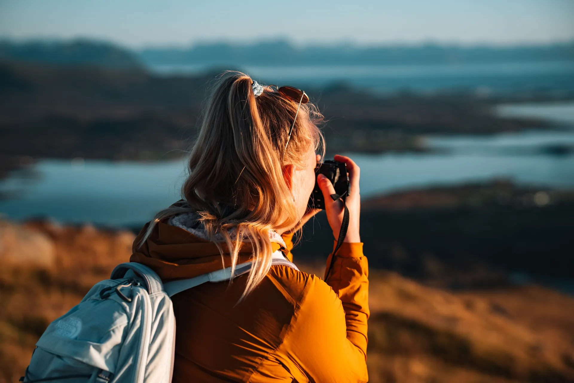 Annina mit Rucksack fotografiert auf dem Skårvågsfjellet, unscharf dahinter Inseln und Wasser im Abendlicht