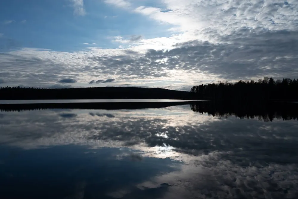 Wolkenspiegelung im spiegelglatten See, links und rechts dunkle Waldränder
