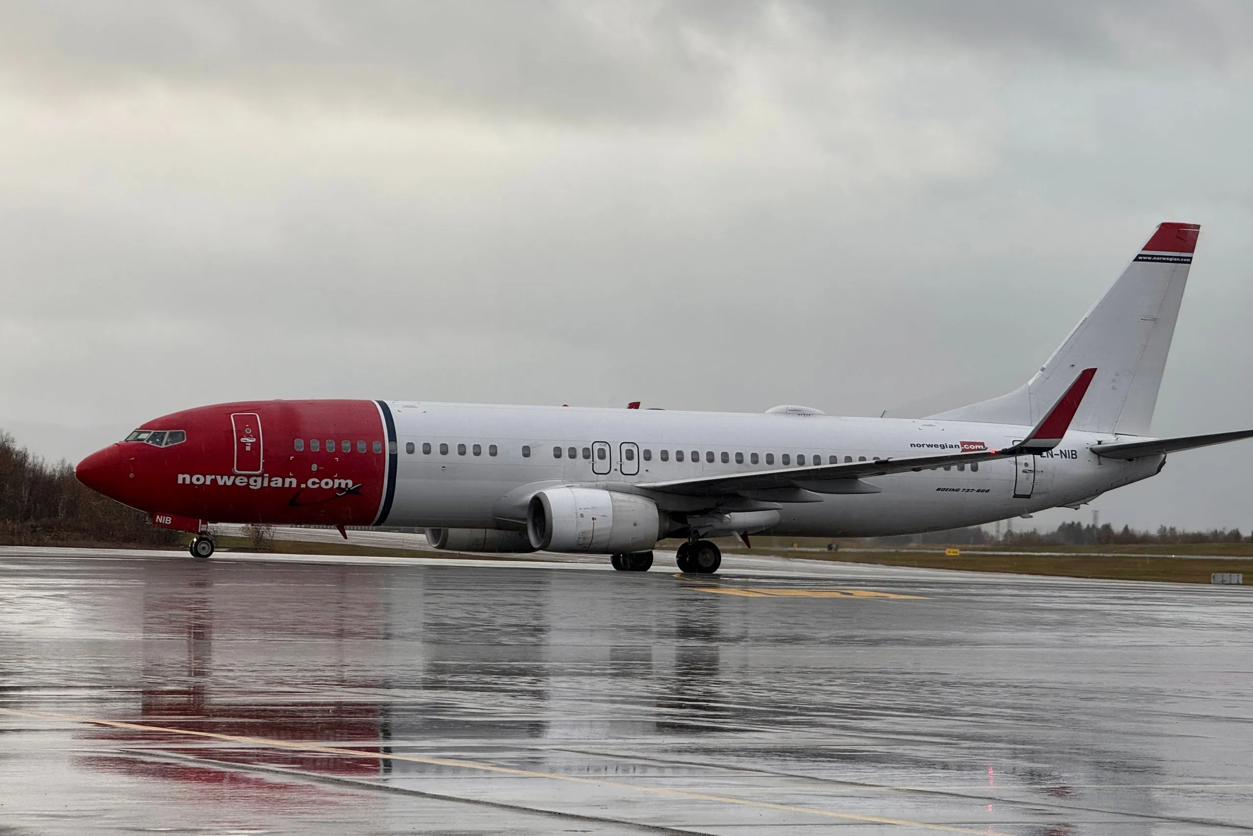 Unsere Norwegian-Maschine, eine Boeing 737 mit roter Nase, auf dem regennassen Vorfeld des Flughafens Evenes unter grauem Himmel