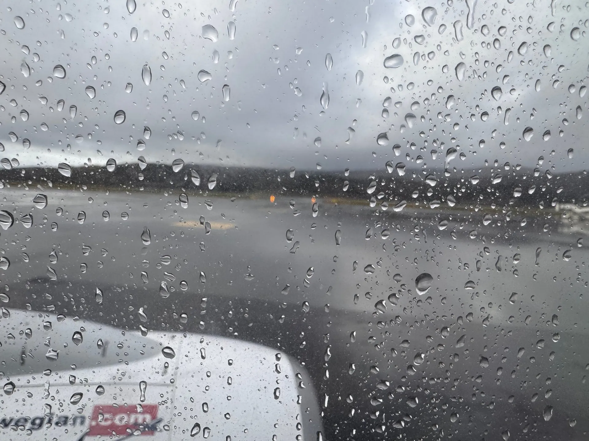 Regentropfen auf dem Fenster, darunter das Triebwerk mit dem Schriftzug norwegian.com, am Flughafen Evenes