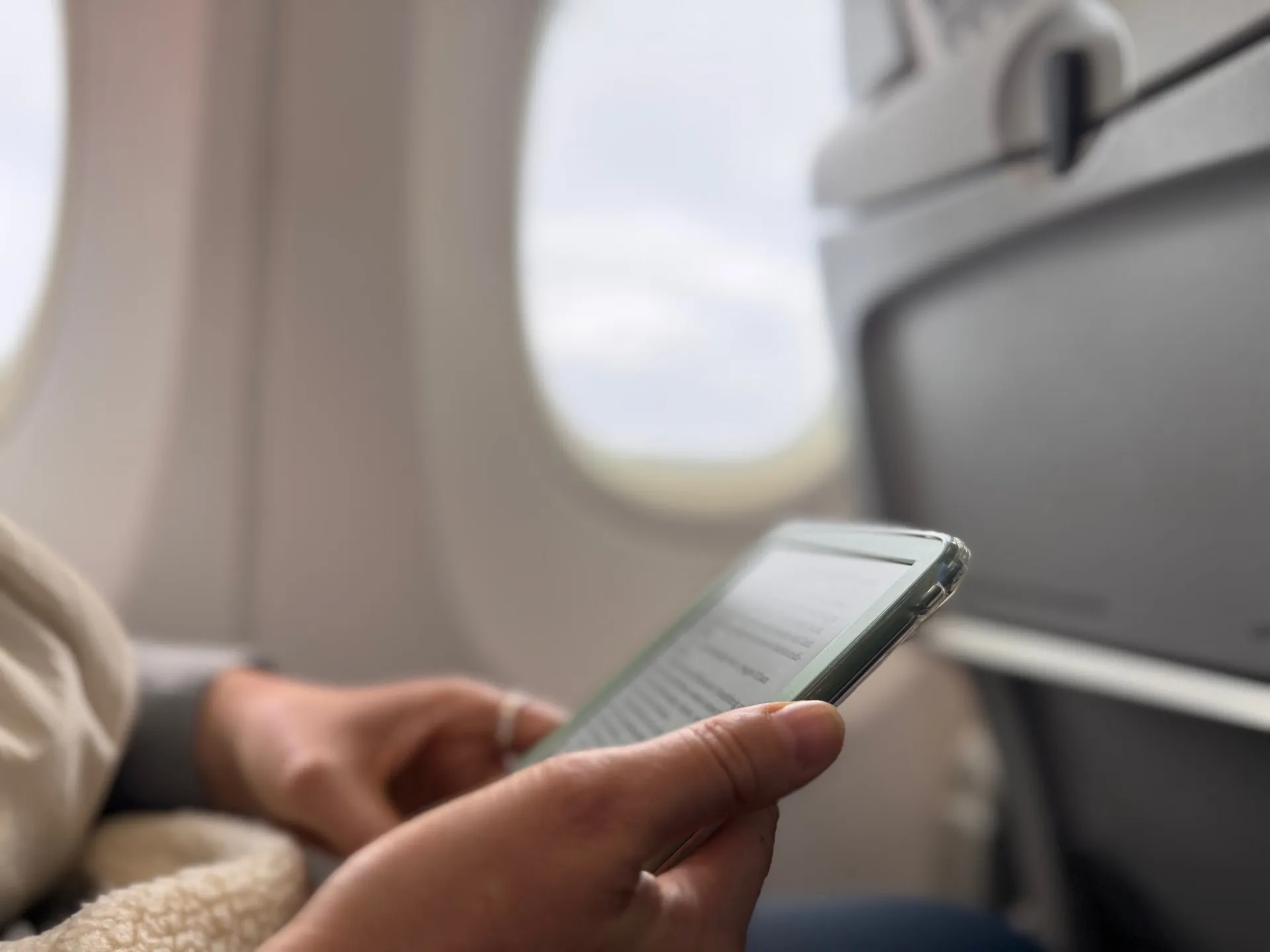 Annina liest auf dem Flug nach Basel auf ihrem E-Book-Reader, im Hintergrund das Fenster und die Rückenlehne des Sitzes vor ihr