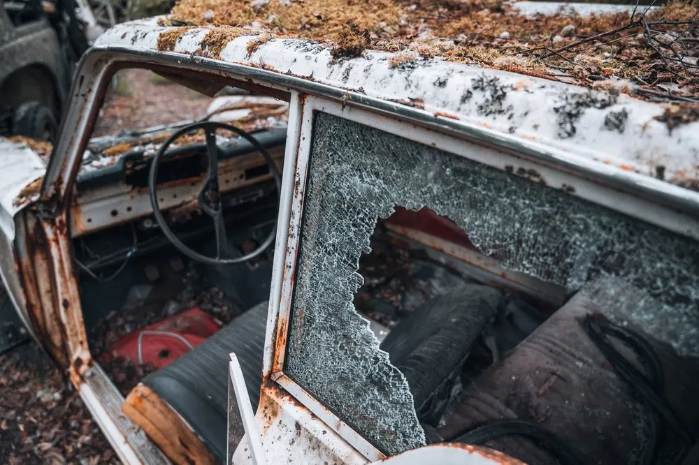 A shattered side window on a white wreck, steering wheel and seats behind it