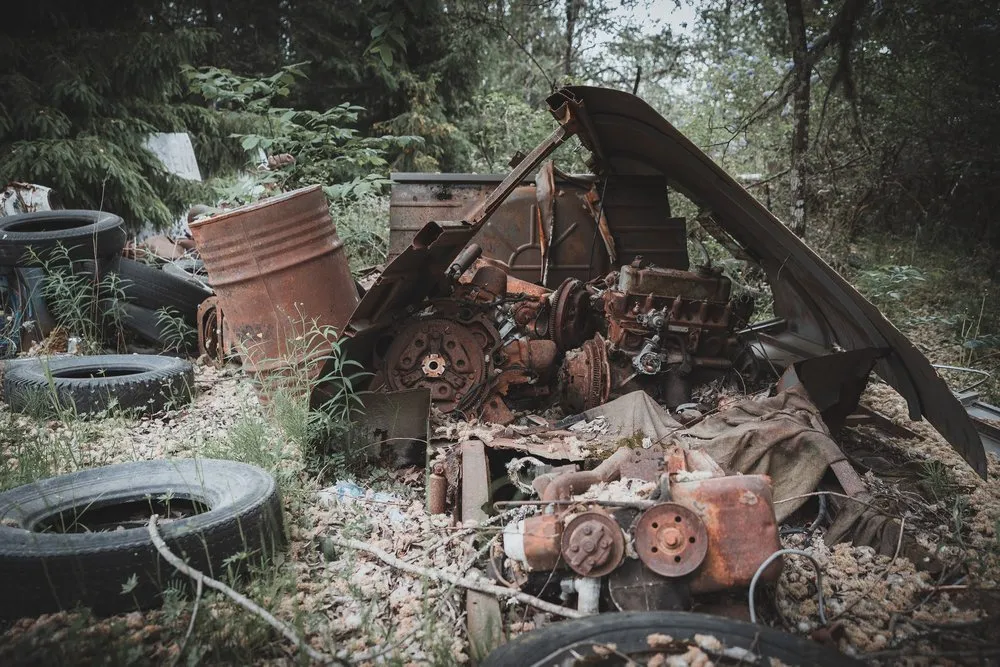 Rusty engine parts, tyres and a barrel lie scattered on the forest floor