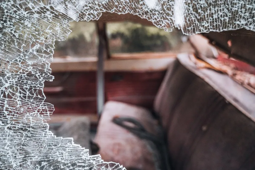 Shattered glass in the foreground, behind it a blurred car seat in the reddish interior