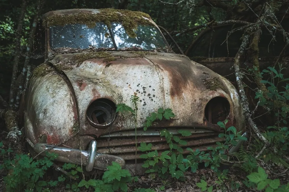 Front view of a moss-covered wreck with round headlights and a rusty radiator grille