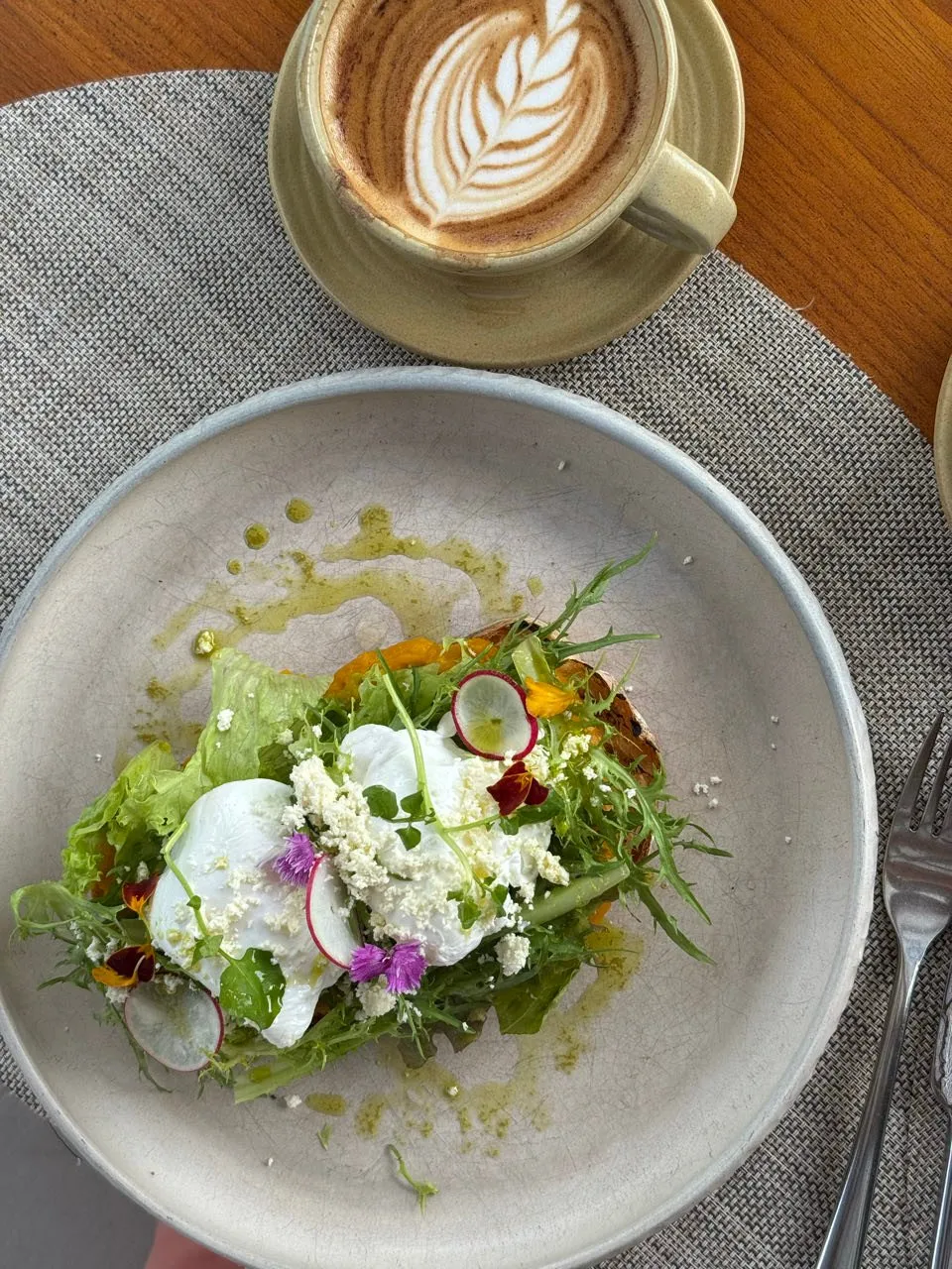Salat mit Radieschenscheiben, essbaren Blüten und weissen Bröseln auf einem Teller, dazu ein Cappuccino mit Blattmuster