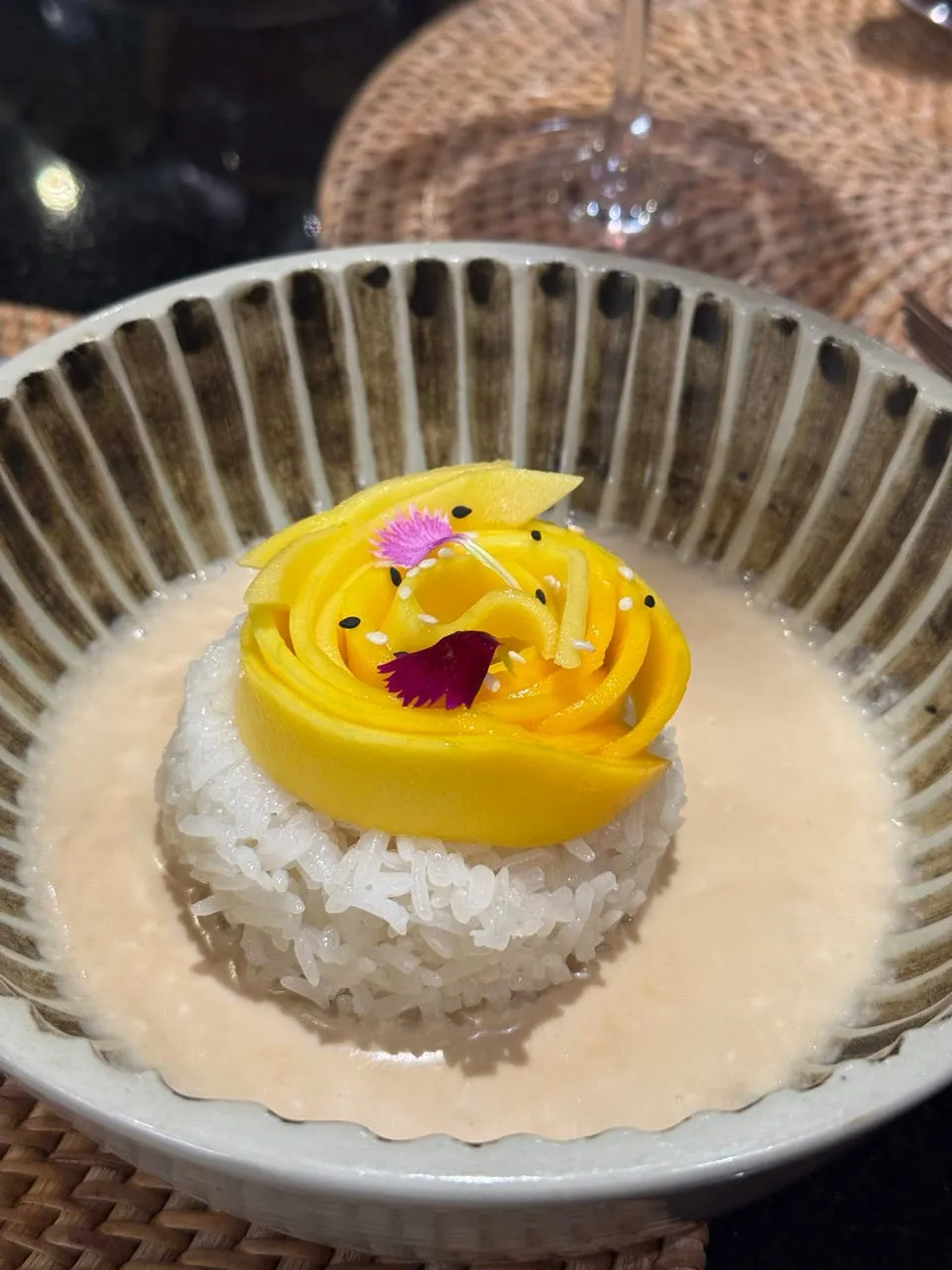 Reis in heller Sauce in einer gestreiften Schale, darauf eine Rose aus Mangoscheiben mit Sesamkörnern und zwei Blüten