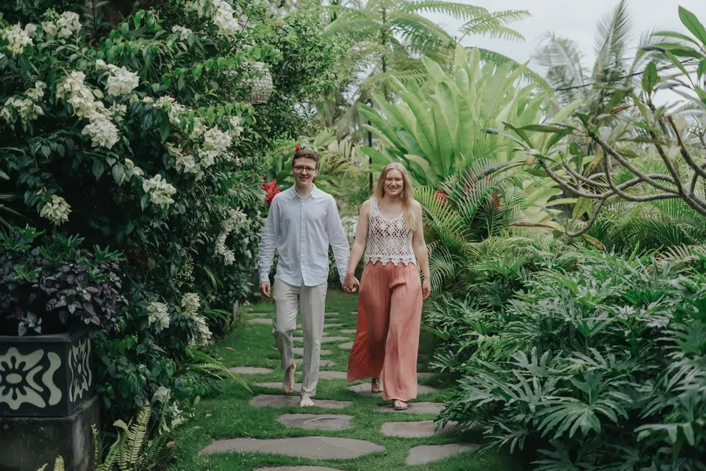 The two of us walk hand in hand over stepping stones through a lush garden with white flowers and large leaves