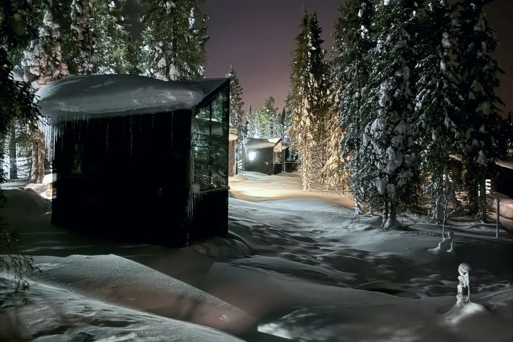 The glass igloo in the night forest with faint northern lights above