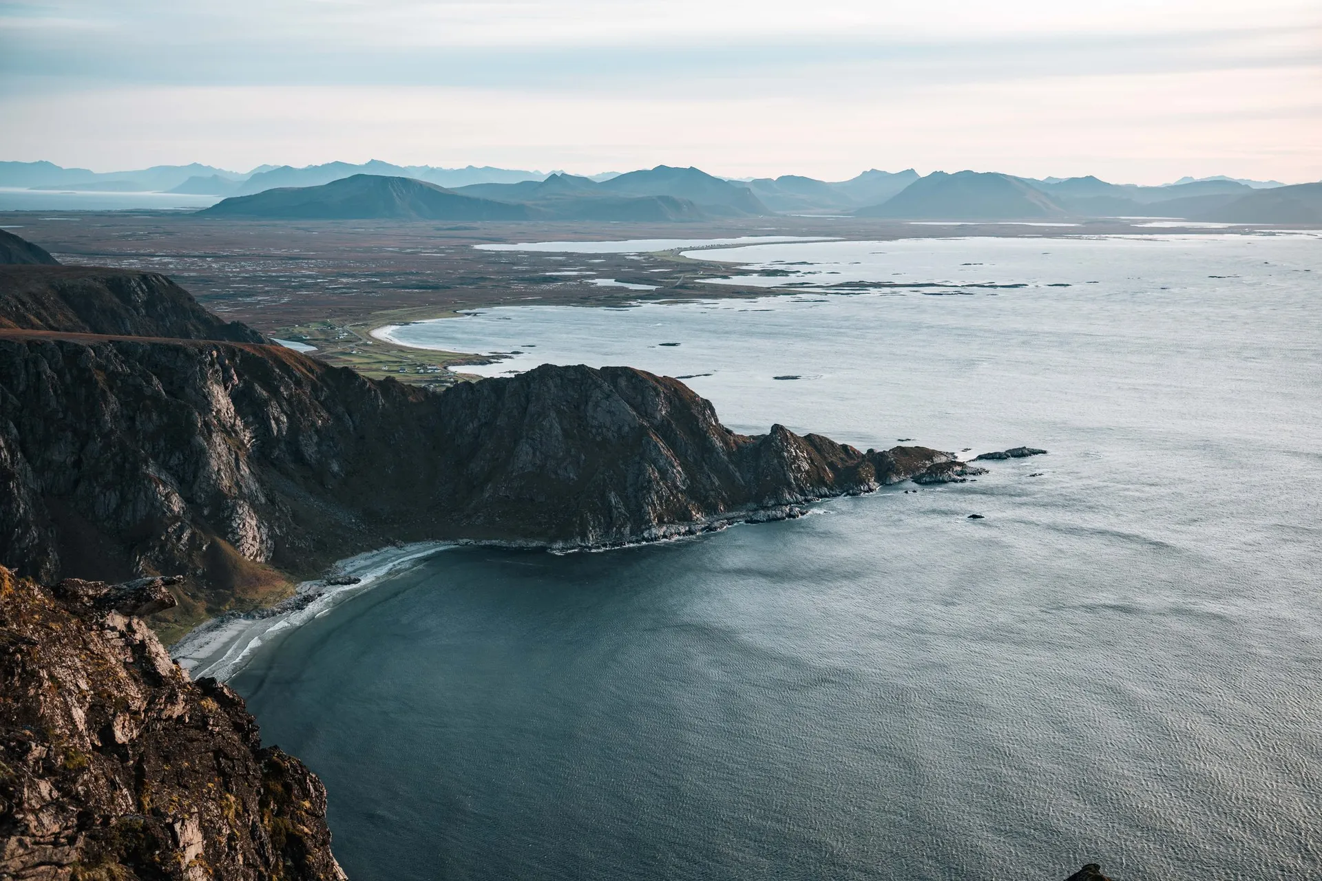 Felsige Klippen ziehen sich zu einer Bucht mit hellem Strand hinunter, vom Måtind aus