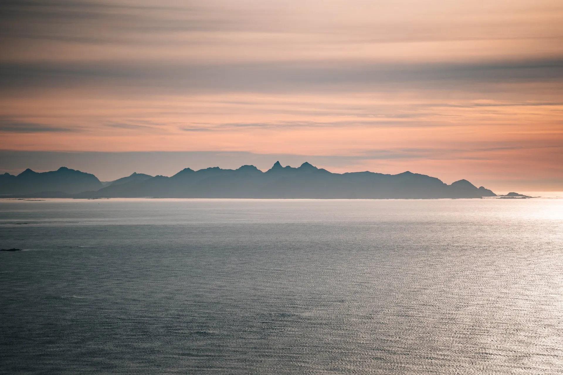 Ein Streifen gezackter Berge am Horizont unter rosa Abendwolken, vom Måtind aus