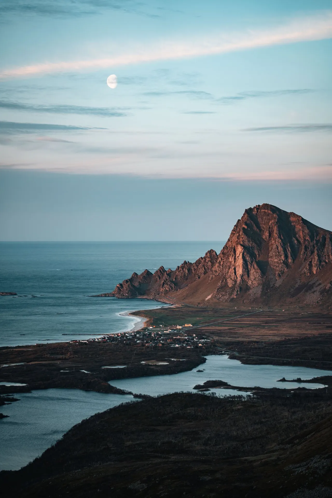 Der Mond über einem rötlich beleuchteten Berg am Meer, beim Abstieg vom Måtind
