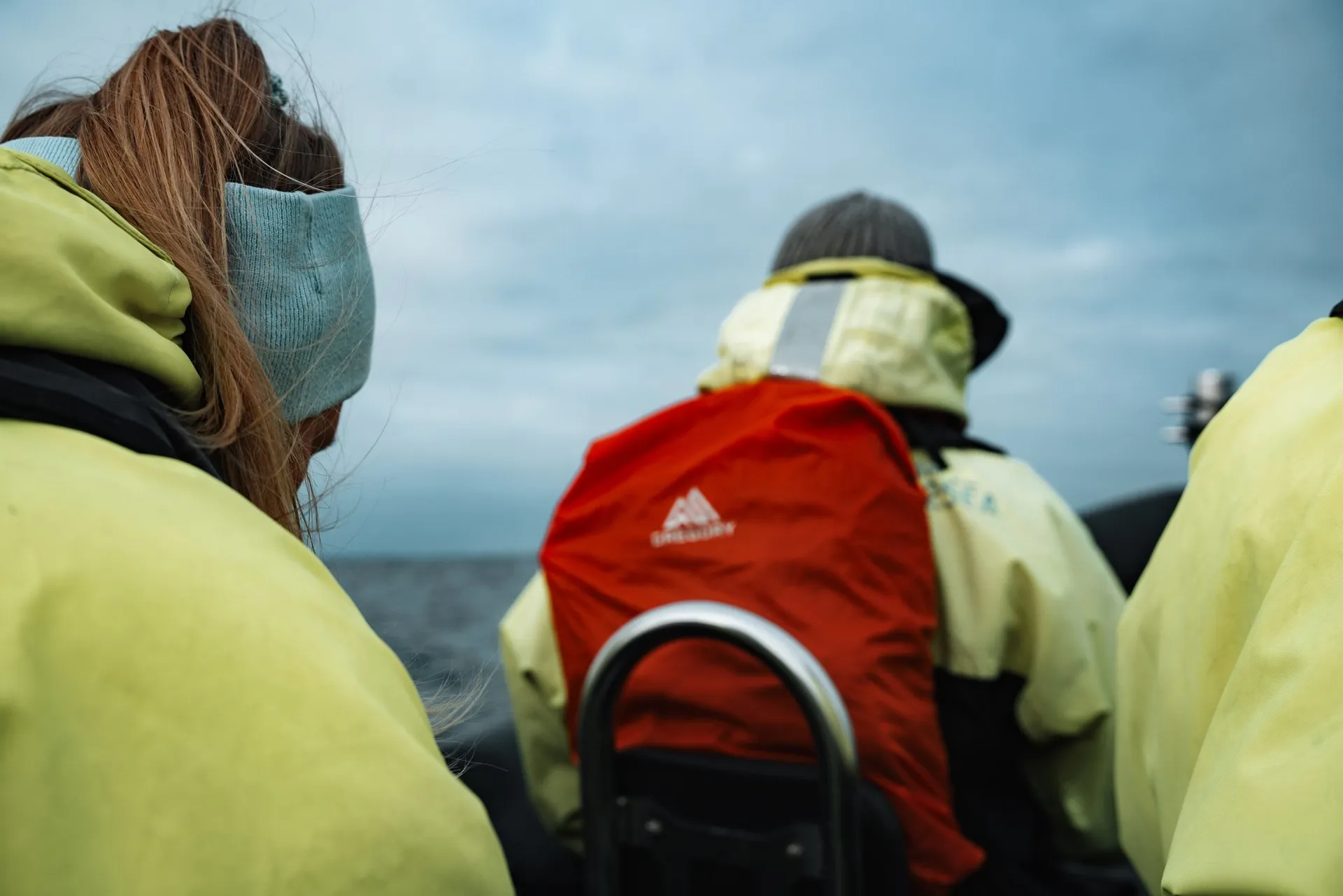 Annina und Mitfahrende in neongelben Thermoanzügen auf den Sitzen des RIB-Boots vor Andenes, einer mit rotem Rucksack