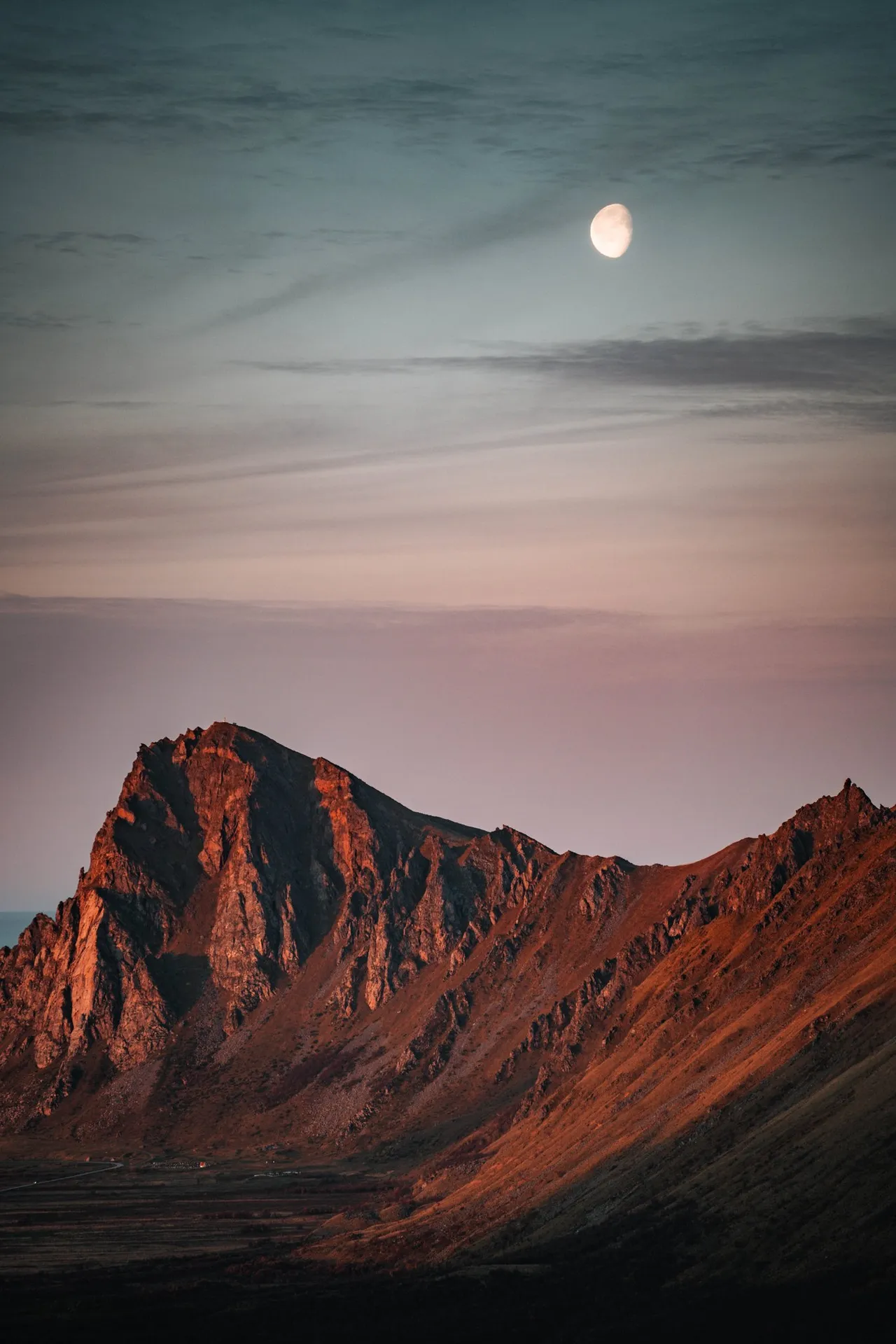 Der Mond am rosa Himmel über einem Berg im letzten Licht, beim Abstieg vom Måtind