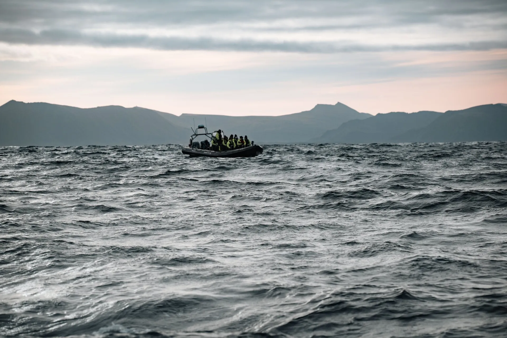Das zweite RIB-Boot voller Leute in neongelben Anzügen auf den Wellen vor Andenes, dahinter die Berge von Andøya