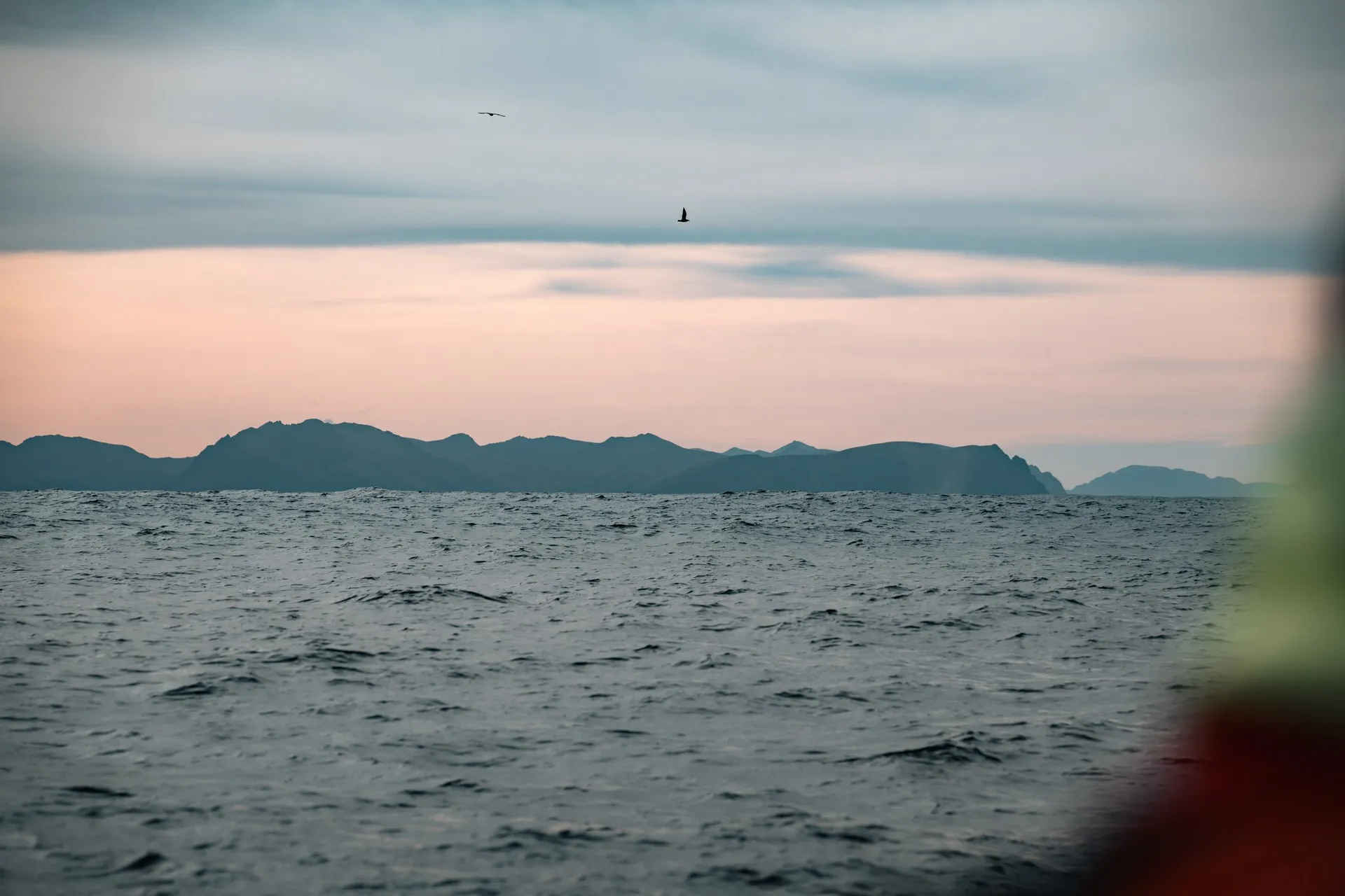 Die Berge von Andøya unter einem rosa Streifen Himmel über dem grauen Meer, auf der Rückfahrt nach Andenes