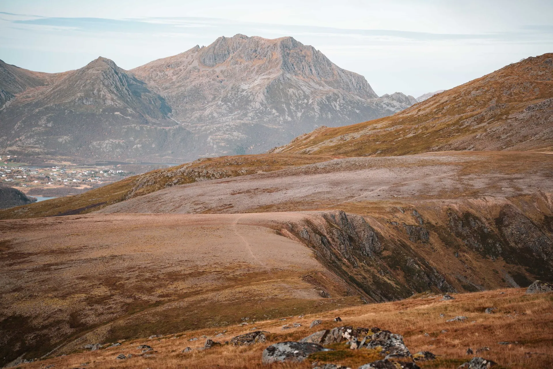 Eine weite Hochebene mit Herbstgras am Weg auf den Vetten, dahinter spitze Berge und eine Siedlung am Wasser