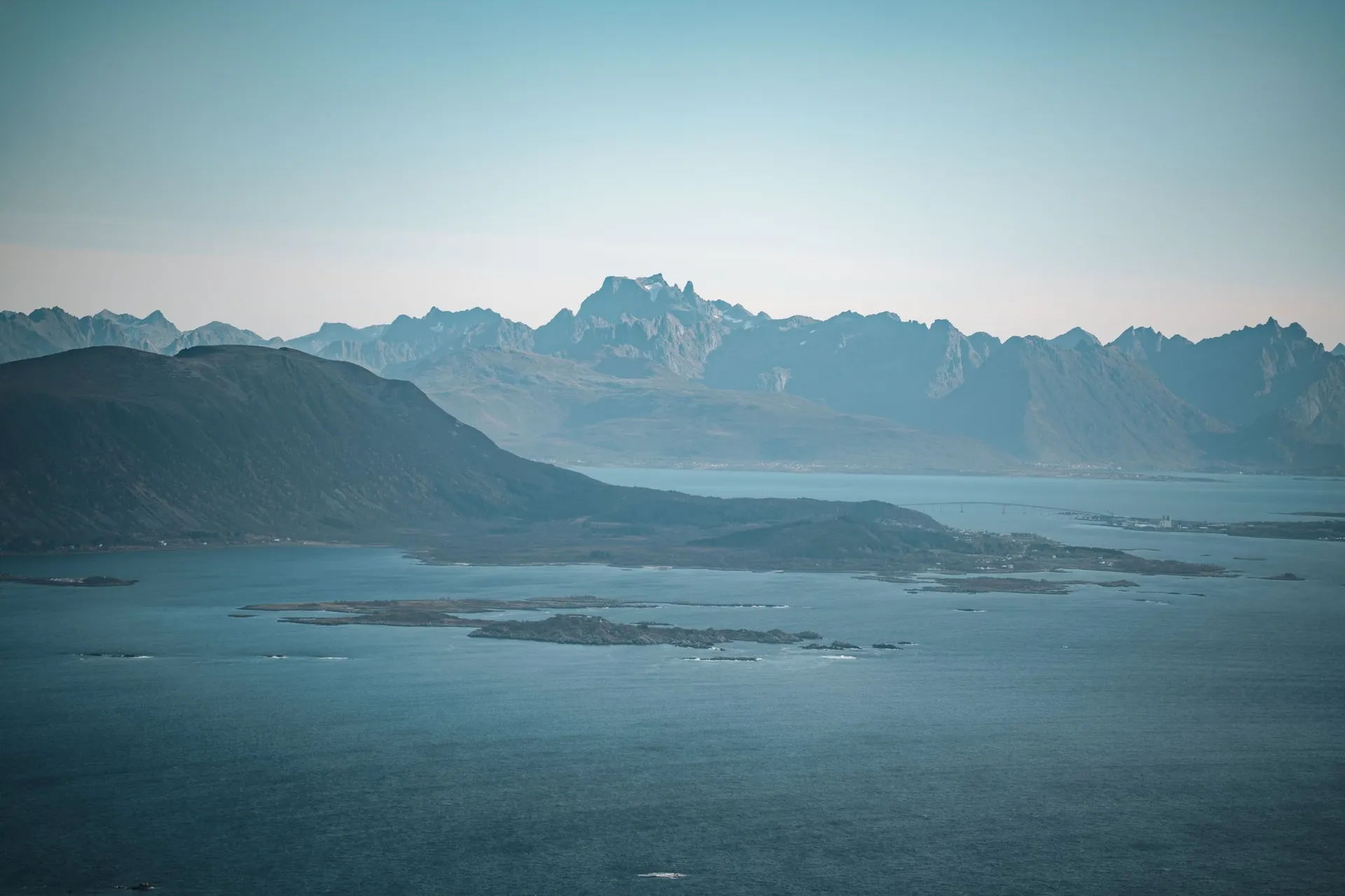Die Berge der Lofoten am Horizont über dem Meer, davor eine dunkle Landzunge, vom Vetten aus