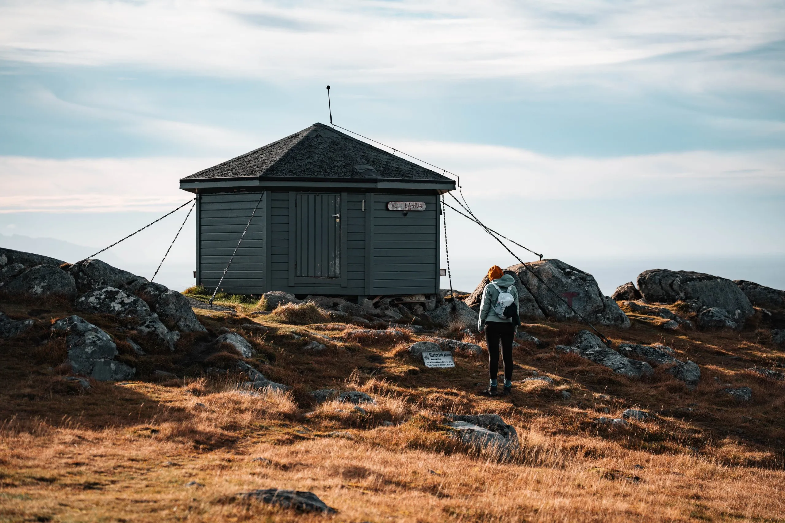 Die kleine Hütte Vettenbua auf dem Gipfel des Vetten, Annina geht mit Rucksack auf sie zu, ringsum Felsen und Herbstgras