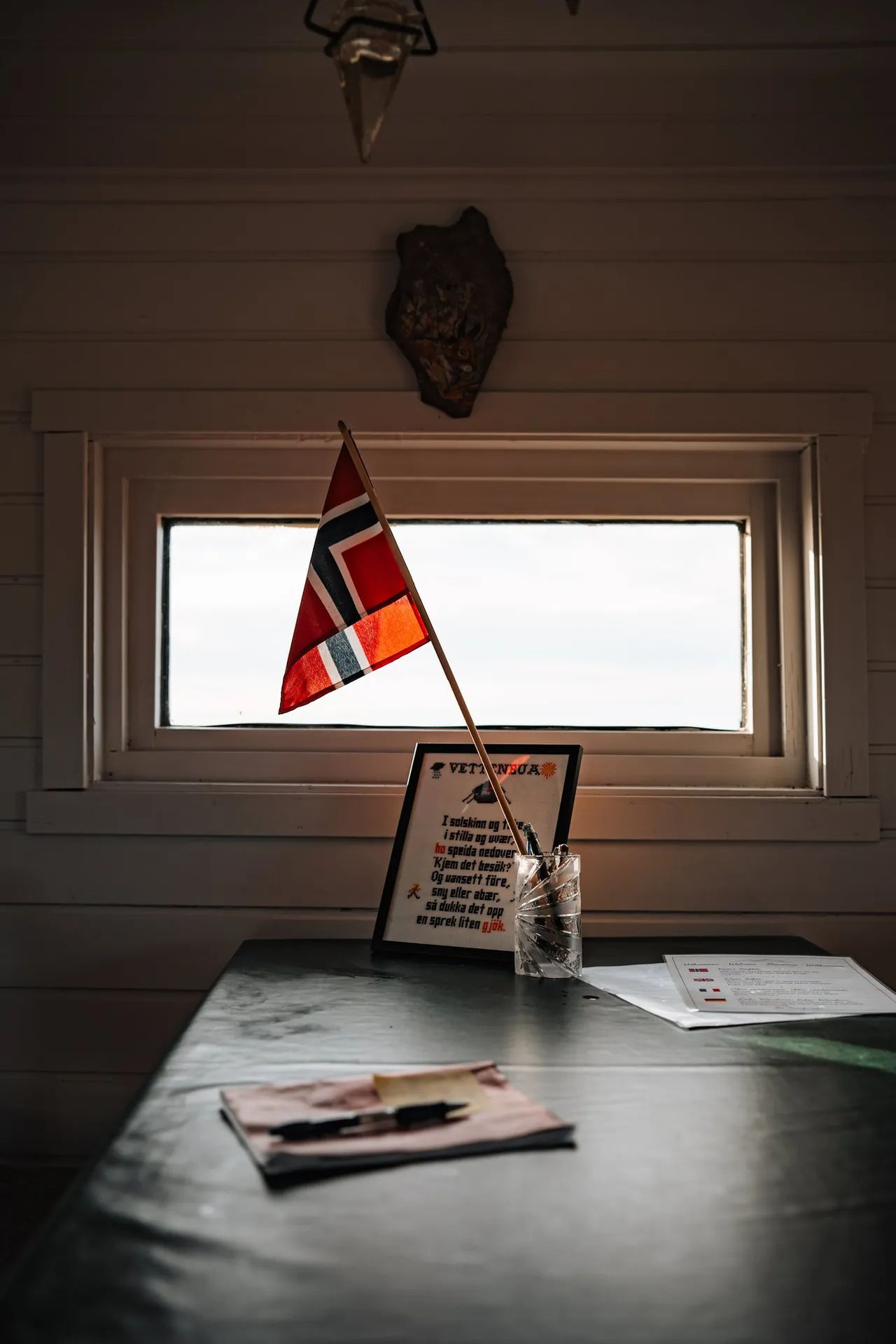 Im Innern der Vettenbua ein Tisch unter einem kleinen Fenster mit einer norwegischen Fahne