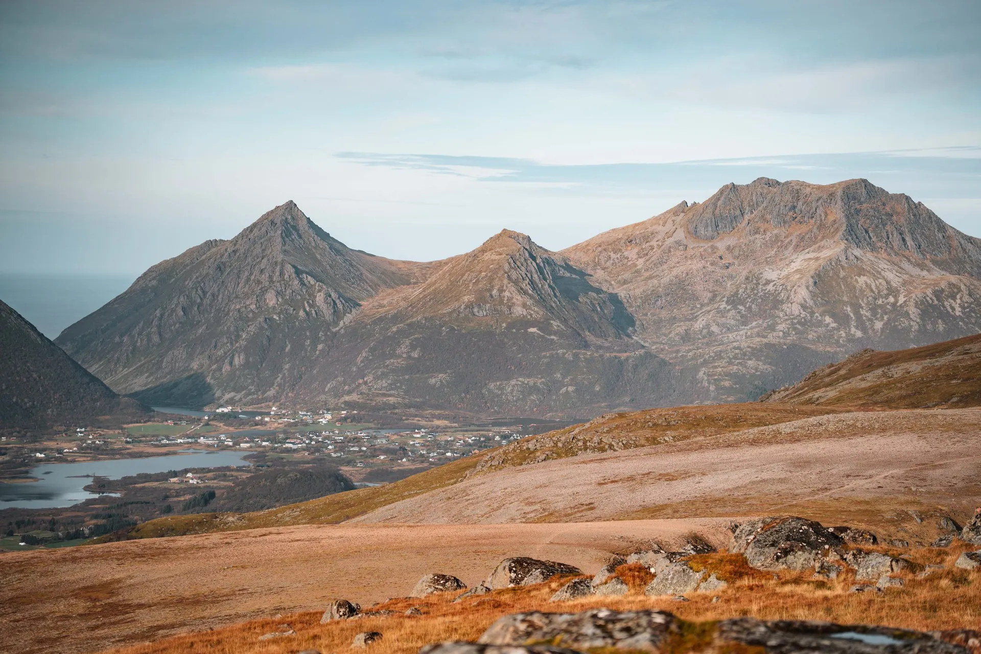 Spitze Berge über einer Siedlung am Wasser, vorne die Hochebene am Vetten mit Gras und Steinen