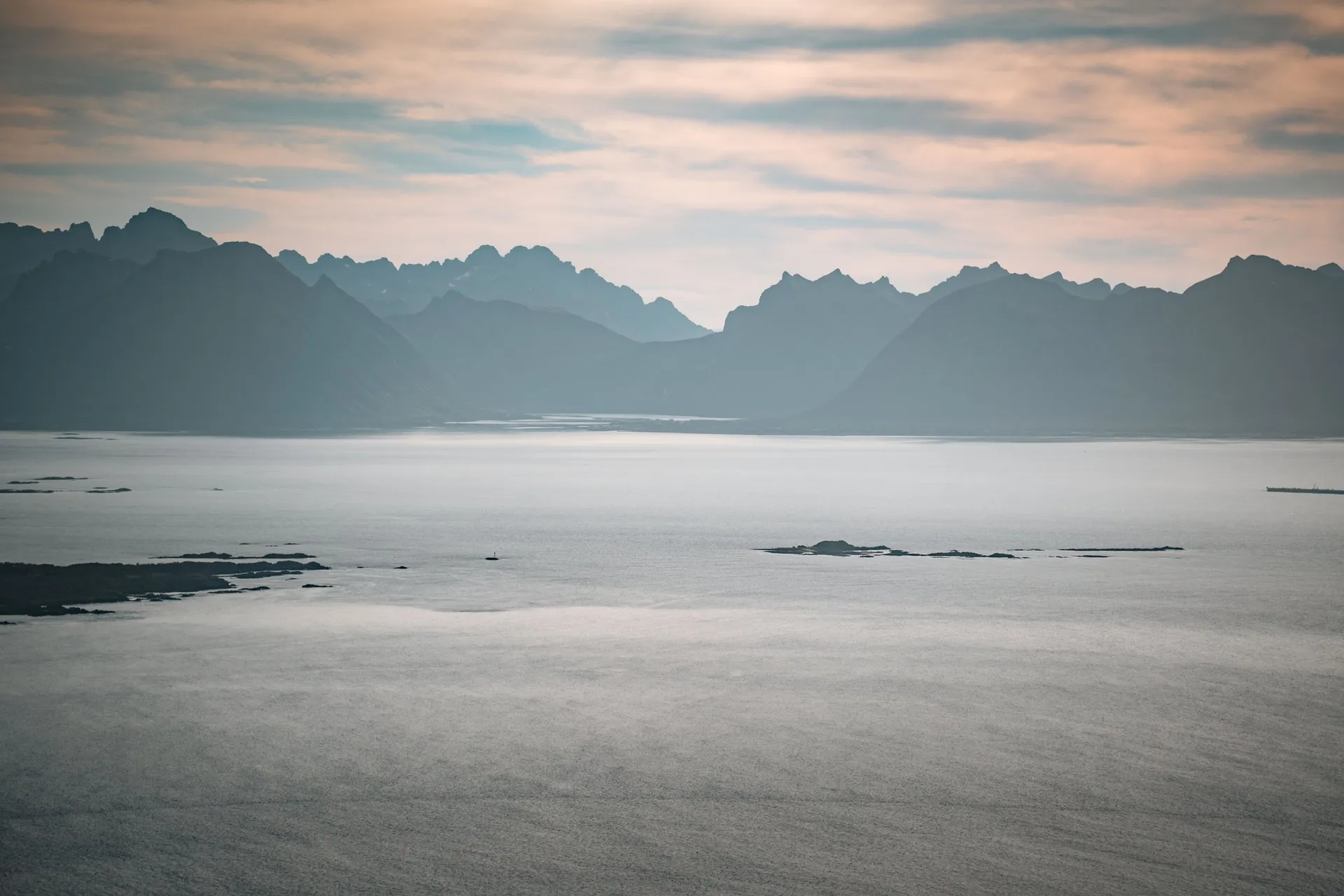 Am Horizont die gezackten Berge der Lofoten über dem ruhigen Meer, davor ein paar flache Inseln, vom Vetten aus