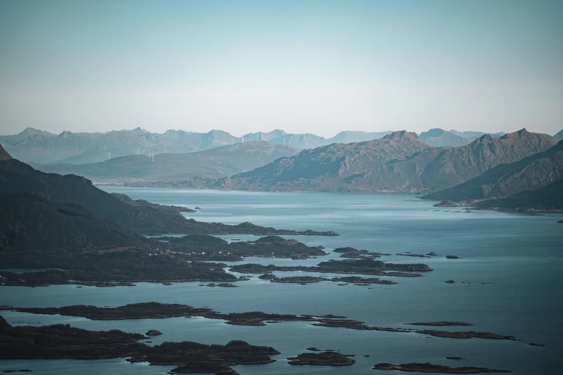 Inseln und Felsbänke in einem Fjord, dahinter Bergketten im Dunst, vom Vetten aus