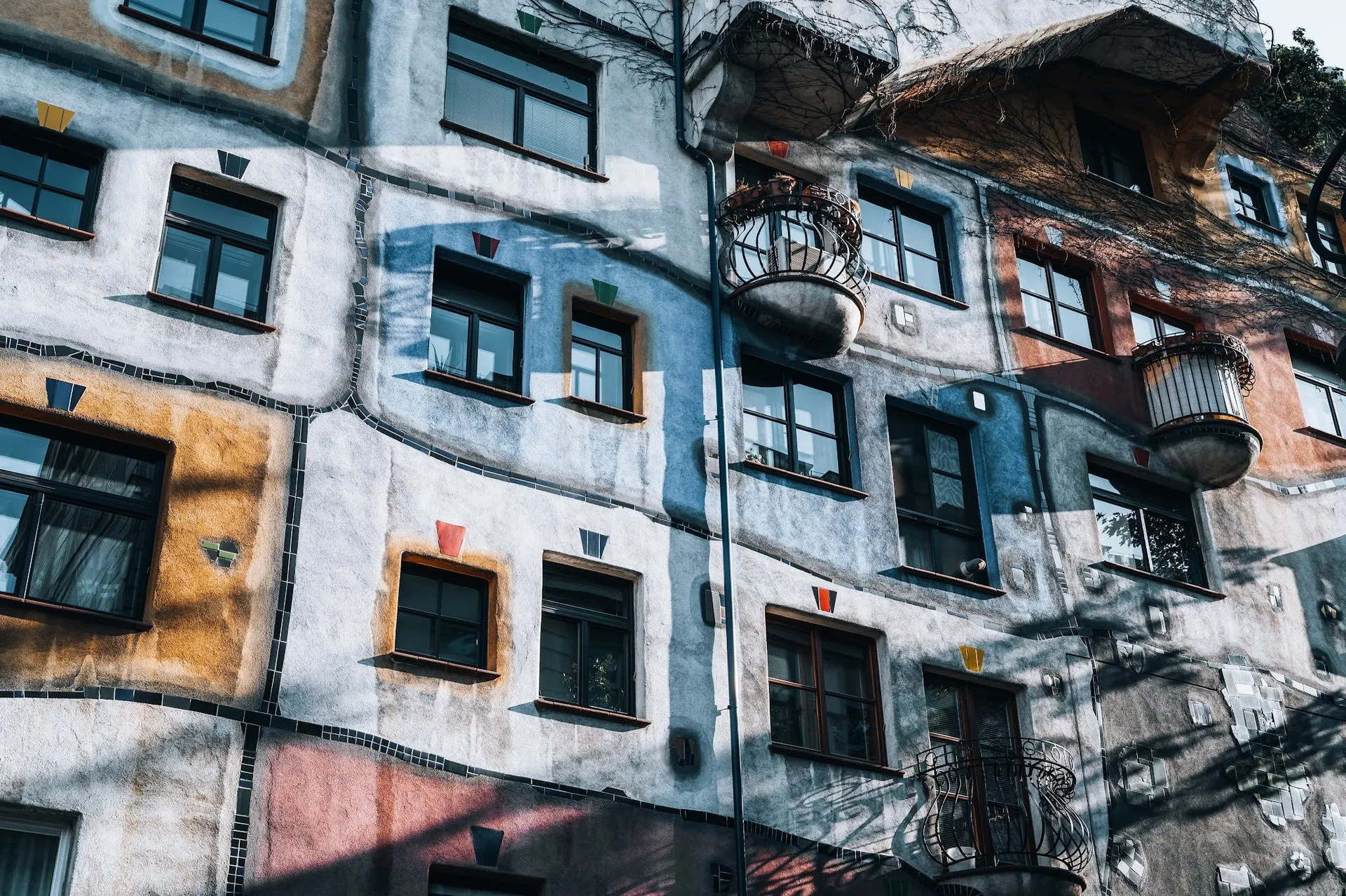 Bunte Hausfassade mit unregelmässig gesetzten Fenstern, farbigen Flächen, runden Balkonen und wellenförmigen dunklen Linien