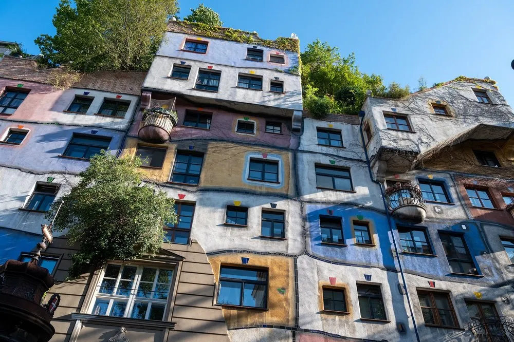 The Hundertwasser House seen from the street, on the left a tree in front of the façade, on the right blue and ochre panels