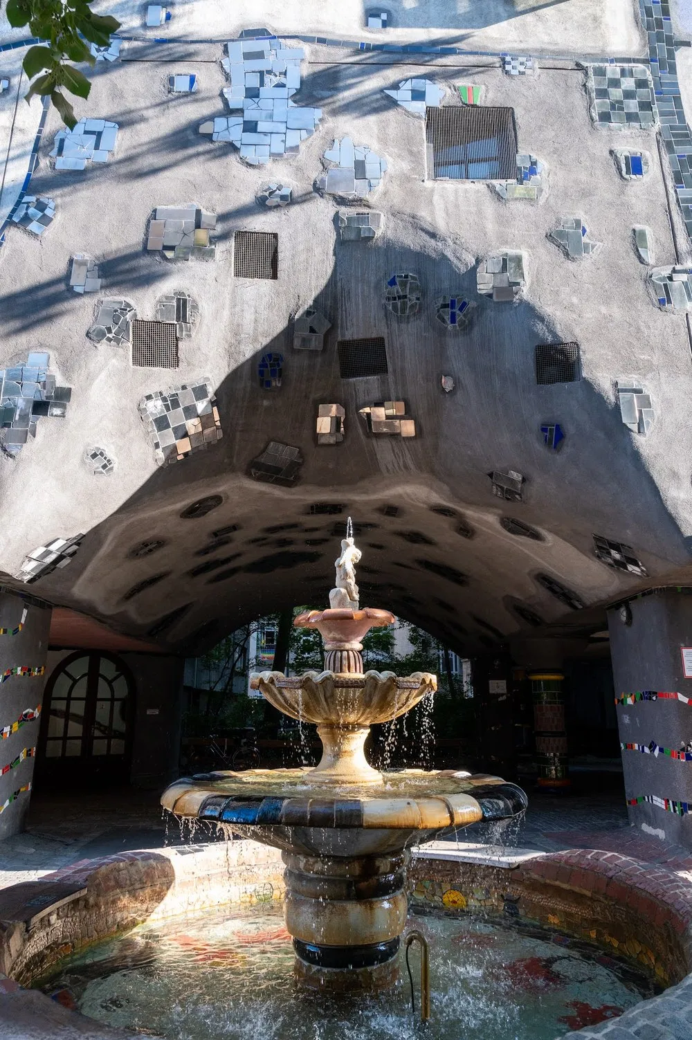 Fountain with a stepped basin under a vaulted passage whose ceiling is decorated with mosaic panels and small windows