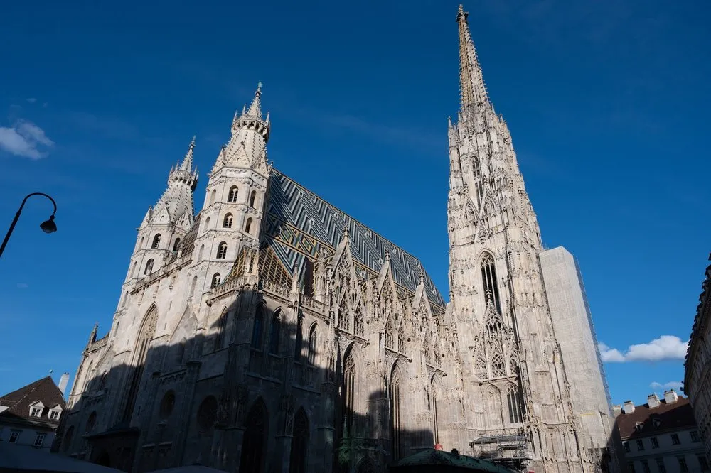 St. Stephen's Cathedral seen from below, with its patterned tiled roof and tall tower against a deep blue sky