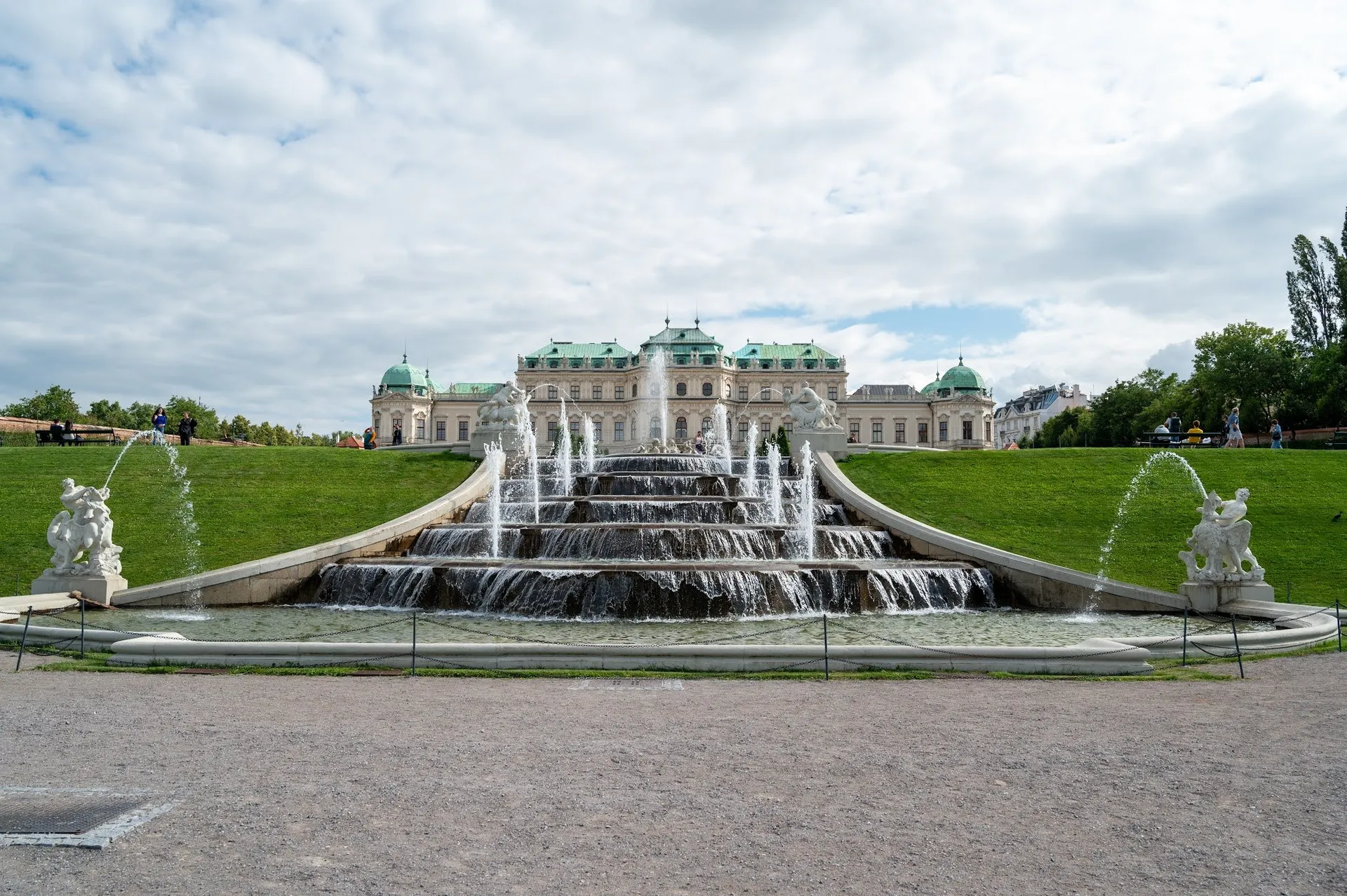 The water cascade with several steps and fountains, statues on the left and right, in the background the palace under a cloudy sky