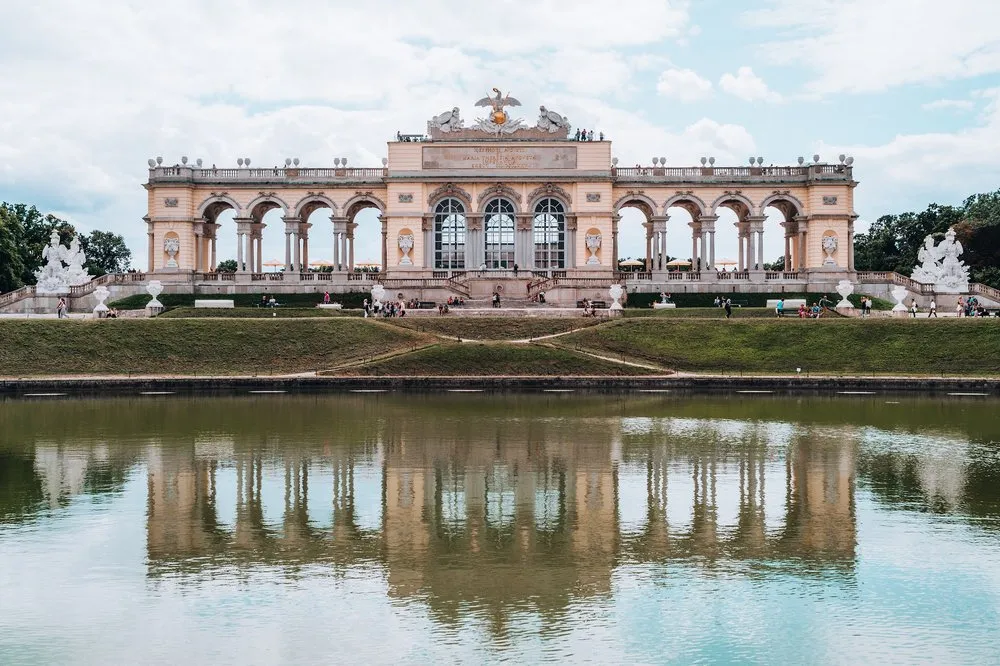 The Gloriette with its arches and white statues, reflected in the pool of water in front of it