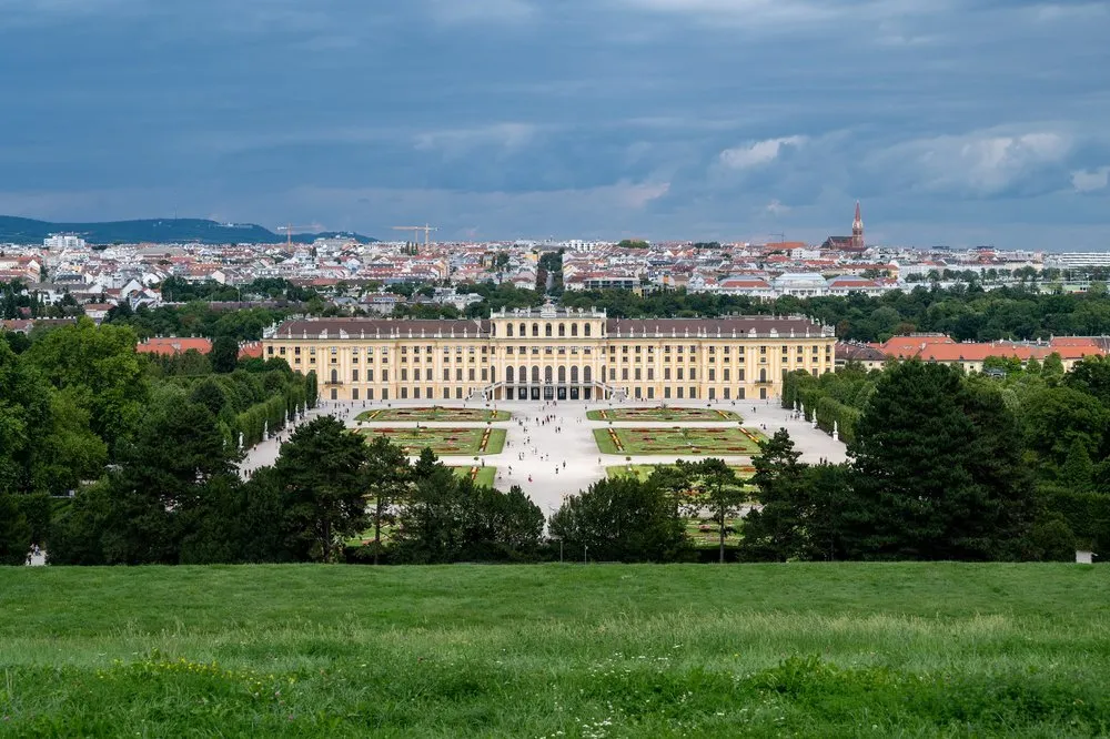Blick von einer Wiese hinunter auf das gelbe Schloss und den Garten, dahinter die Dächer der Stadt