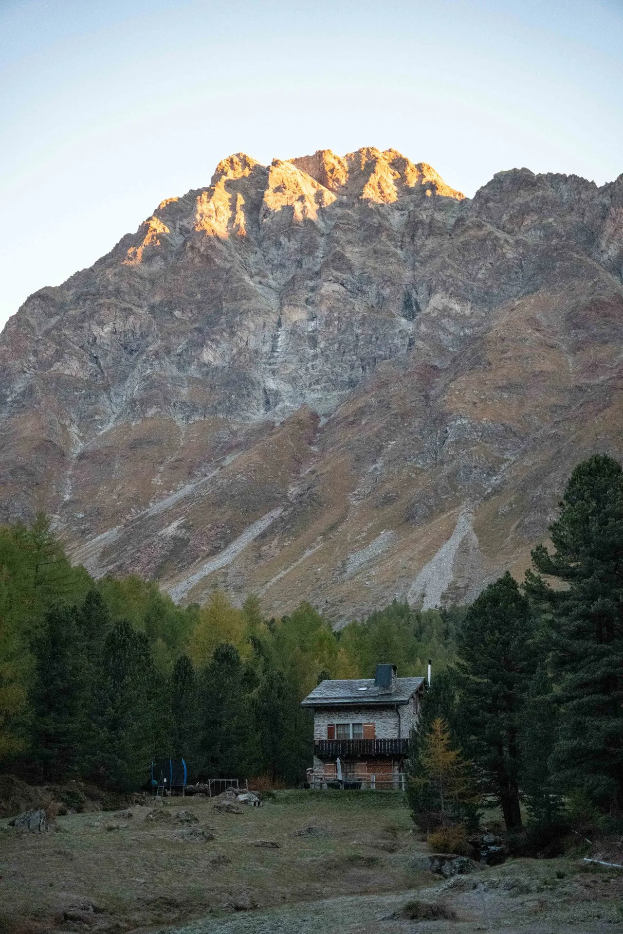 Im ersten Morgenlicht leuchtet nur der oberste Grat über Lungacqua orange, das Steinhaus auf der Wiese davor liegt noch im Schatten